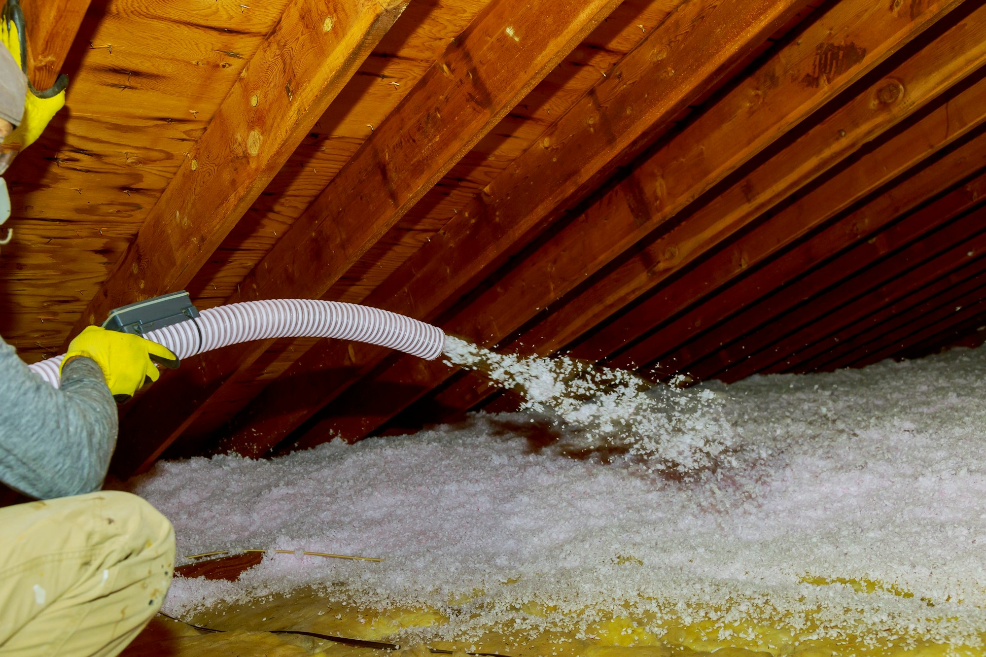 Technician spraying blown Fiberglass Insulation between Attic Trusses foam insulation repair tool in